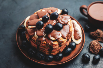 Pancakes with banana, chocolate sauce and grapes in plate, on dark background