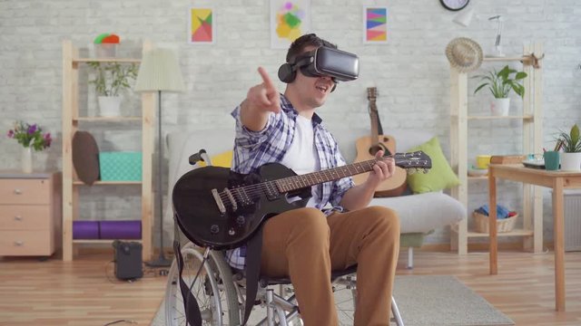 Portrait young man disabled in a wheelchair in virtual reality glasses musician plays the electric guitar