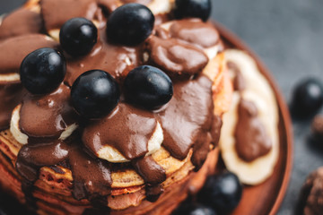 Pancakes with banana, chocolate sauce and grapes in plate, on dark background