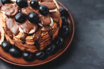 Pancakes with banana, chocolate sauce and grapes in plate, on dark background
