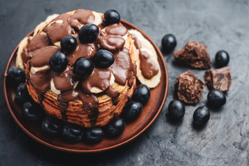 Pancakes with banana, chocolate sauce and grapes in plate, on dark background