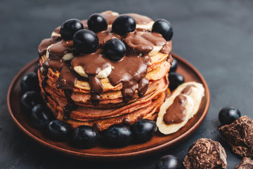 Pancakes with banana, chocolate sauce and grapes in plate, on dark background