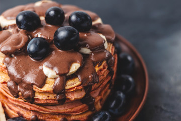 Pancakes with banana, chocolate sauce and grapes in plate, on dark background
