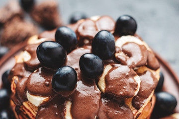 Pancakes with banana, chocolate sauce and grapes in plate, on dark background