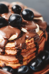 Pancakes with banana, chocolate sauce and grapes in plate, on dark background