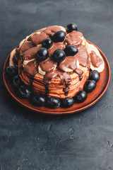 Pancakes with banana, chocolate sauce and grapes in plate, on dark background