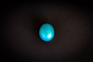 turquoise (blue) painted egg isolated on black background; shiny, marbled, oval-shaped creative object