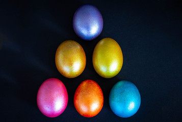 a pyramid of six colorful, shiny neon eggs on a black background from above;  an abstraction on Easter; an unusual, creative