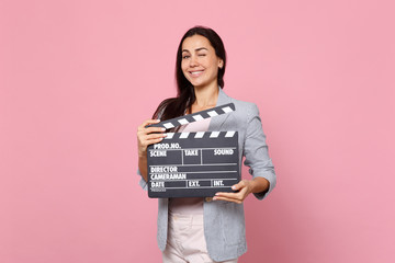 Blinking young woman in striped jacket holding classic black film making clapperboard isolated on...