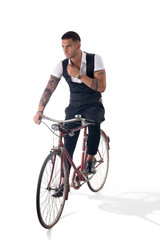 Fototapeta na wymiar Portrait of young tattooed man in elegant clothes riding a bicycle. Studio shot. Full body shot