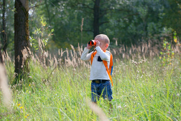 Young explorer watching with binoculars of birds in the high grass