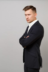 Side view of displeased young business man in classic black suit, shirt holding hands folded isolated on grey wall background in studio. Achievement career wealth business concept. Mock up copy space.