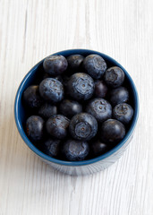 Fresh blueberries in a blue bowl over white wooden background, top view. Close-up.