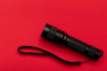 Black pocket electric torch on a red background. Close up.