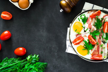 breakfast scrambled eggs tomat bacon and greens on black background