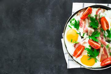 breakfast scrambled eggs tomat bacon and greens on black background