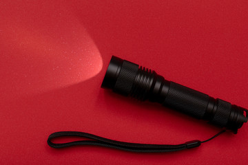 Black pocket electric torch on a red background. Close up.