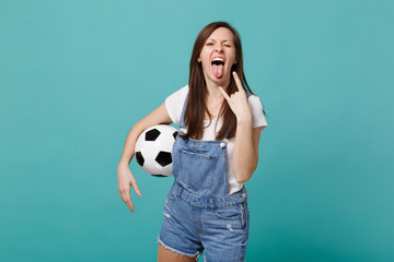 Crazy young woman football fan cheer up support favorite team with soccer ball showing tongue, horns up gesture isolated on blue turquoise background. People emotions, sport family leisure concept.