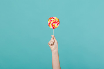 Close up female holding in hand colorful round lollipop isolated on blue turquoise wall background. Proper nutrition or sweets dessert fast food, dieting morning concept. Copy space for advertisement.