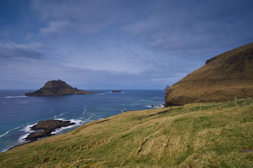 Fototapeta premium Epic colorful landscape of wild nordic or scandinavian coastline without trees with atlantic ocean, mountains, high cliffs in island Vagar in Faroe island taken in sunny, cloudy and windy summer day.