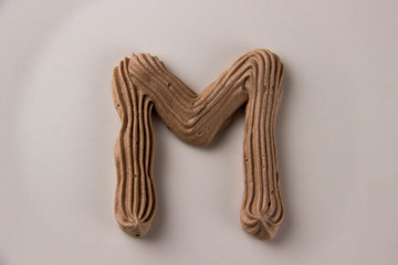 Sweet chocolate letter M drawn with whipped cream on a white plate
