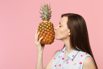 Side view of young woman in summer clothes hold kissing fresh ripe pineapple fruit isolated on pink pastel wall background in studio. People vivid lifestyle relax vacation concept. Mock up copy space.