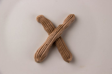 Sweet chocolate letter X drawn with whipped cream on a white plate