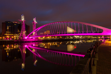 A night view of a pink neon arch bridge over a canal
