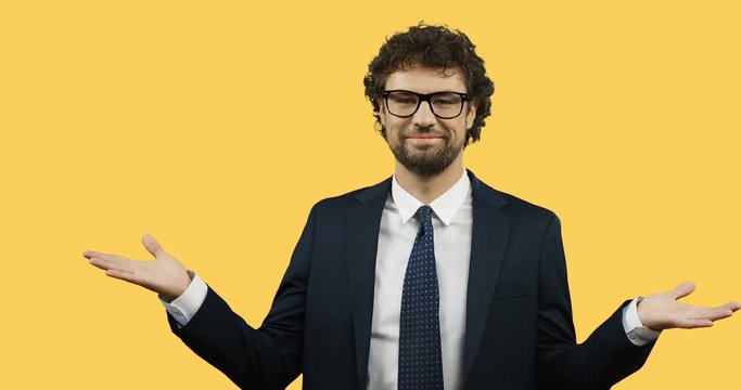 Smiled Caucasian Man In Suit And Tie Doing Gesture With Hands Like I Don't Know Or Whatever On The Yellow Screen Background.