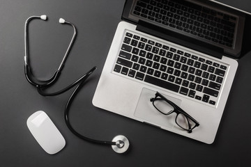 Top view of a doctor's table with notepad and pen stethoscope, laptop, prescription and pills, a cup of coffee on a black background with space for your text
