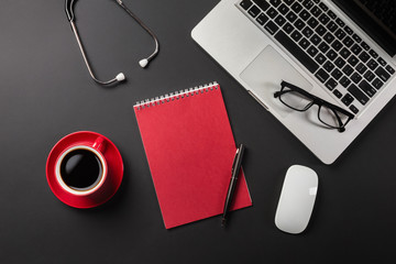 Top view of a doctor's table with notepad and pen stethoscope, laptop, prescription and pills, a cup of coffee on a black background with space for your text