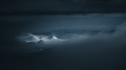 Snowy mountain peaks illuminated in a dark landscape