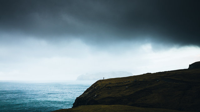 Person stands on a cliff under storm clouds