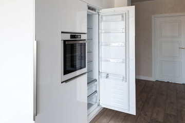 Opened integrated build-in refrigerator in a white glossy kitchen. Perfect way to hide kitchen...