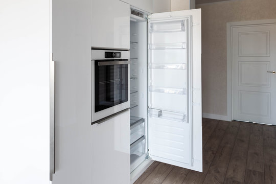 Opened integrated build-in refrigerator in a white glossy kitchen. Perfect way to hide kitchen appliances. 