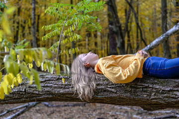 Girl lying on tree trunk in autumnal forest relaxing