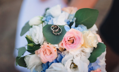 Two gold wedding rings lie on bride bouquet from white and pink roses.
