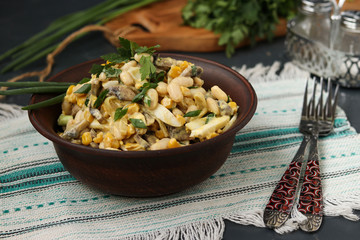 Salad with beans, corn, eggs and champignons in a brown bowl over a dark background
