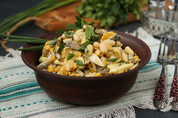 Salad with beans, corn, eggs and champignons in a brown bowl over a dark background