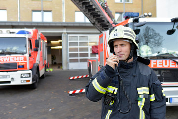 Firefighter standing on yard at fire engine using walkie talkie