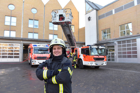 Portrait of smiling firefighter in front of fire engine with colleagues in background