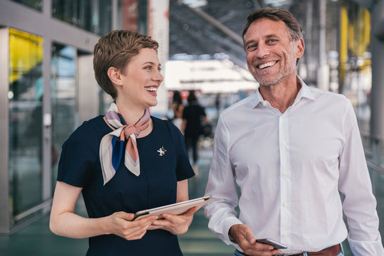 Happy airline employee with tablet and passenger with cell phone at the airport