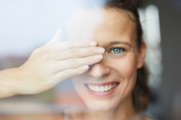 Portrait of laughing young woman behind windowpane covering her eye