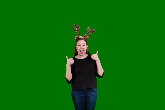 Youthful lady wearing reindeer antlers gesturing two thumbs up on green screen background