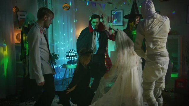 Halloween Costume Party: Group of Monsters Dancing in Decorated Room with Disco Ball Lights. Zombie, Vampire, Mummy, Beautiful Witch, She Devil, Death, Little Bloody Bride and Bat. In Slow Motion
