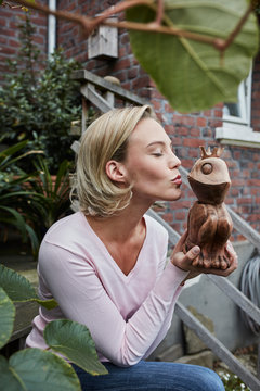 Young woman sitting on stairs kissing wooden frog prince