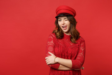 Portrait of blinking sexy young woman in lace dress, cap looking camera showing tongue isolated on bright red wall background in studio. People sincere emotions lifestyle concept. Mock up copy space.