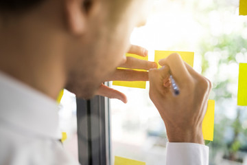Businessman writing on yellow post-its on window
