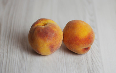 Two peaches on the light wooden background