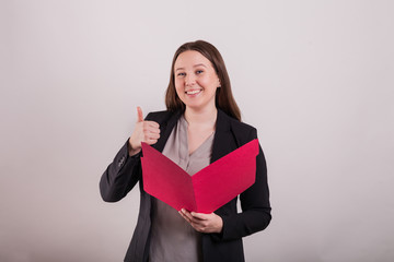 Young business woman wearing suit holding red file folder giving a thumbs up nice smile on solid background